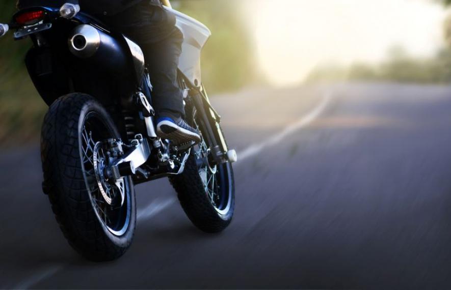 Motard roulant sur une route sinueuse avec un arrière-plan ensoleillé.